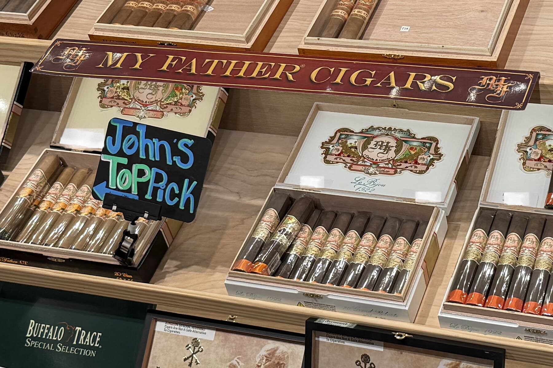 A handwritten sign reading John’s Top Pick, pointing at a box of cigars under the My Father Cigars sign