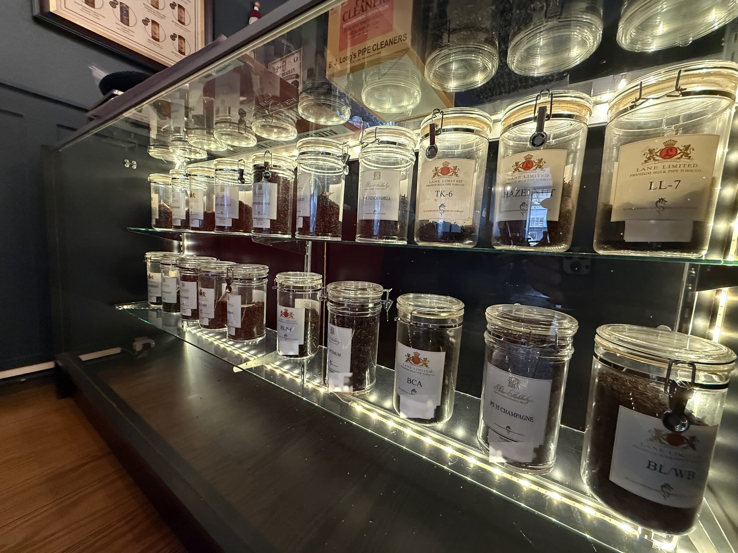 Jars of Lane Limited and Peter Stokkebye bulk pipe tobacco in a lit glass case