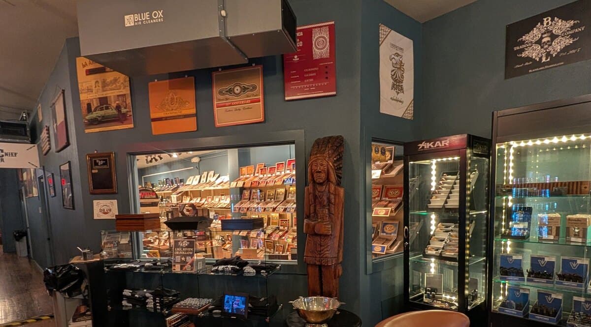 A carved wooden cigar-store figure beside the lighter cases and the window into the humidor