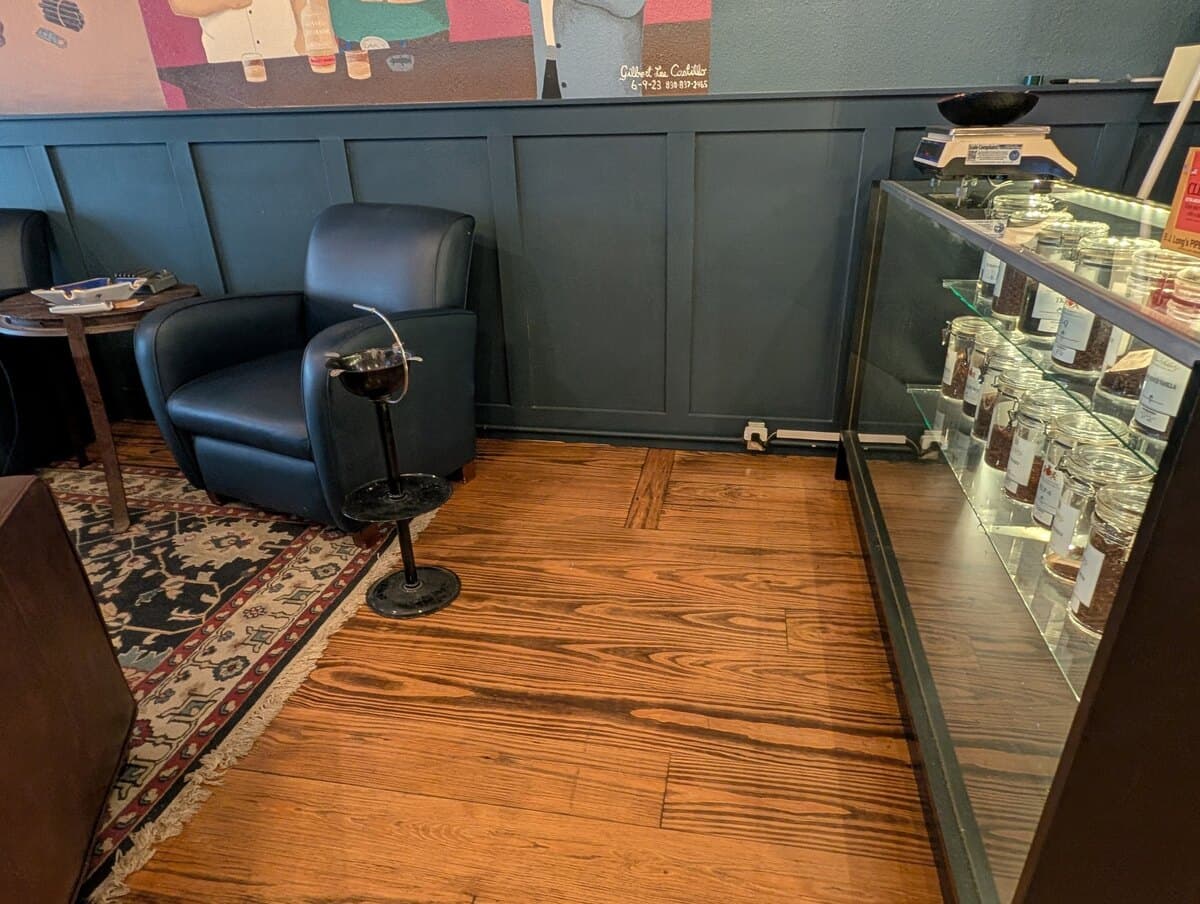 Jars of bulk pipe tobacco in a lit glass case beside a leather armchair